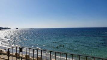Blick auf die Küste mit blauem Himmel, einem Strand und einer Straße mit parkenden Autos.