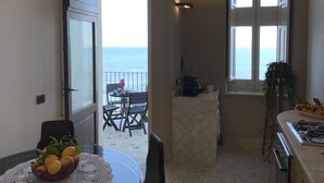 A balcony with a view of the sea, a dining area with a table and chairs, and a kitchen area with a gas stove. - Large apartment for exclusive use on the sea (Trapani)