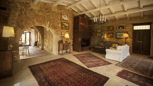 A rustic room with stone walls, a fireplace, a white sofa, and multiple rugs. - Ancient Mint center Sicily (Pietraperzia (EN) Sicili)