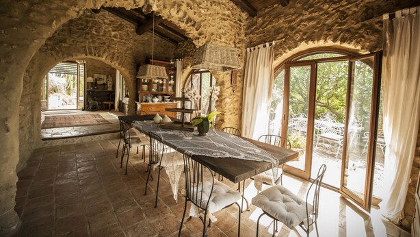 An interior with a rustic stone wall, a wooden table with chairs, and a view of the outdoors through large windows. - Ancient Mint center Sicily (Pietraperzia (EN) Sicili)