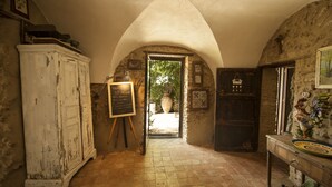 A rustic interior with a stone archway leading to a garden, a white cabinet, a chalkboard, and a wooden table with a decorative plate. - Ancient Mint center Sicily (Pietraperzia (EN) Sicili)