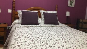 Una cama con colcha estampada, dos almohadas, cabecero de madera y una pared con un cuadro floral.