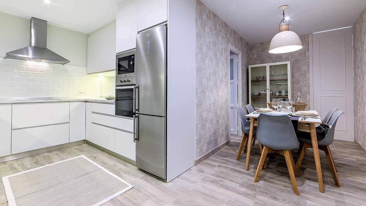 A modern kitchen with stainless steel appliances, a dining area with a table and chairs, and a textured wall.