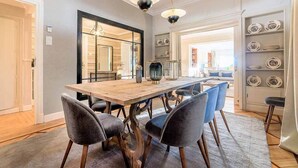 Un comedor con una mesa de madera, seis sillas y una alfombra. Hay una estantería con platos y un espejo en la pared.