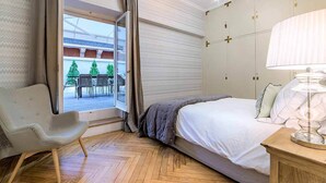 Una habitación de hotel con cama, una silla, una lámpara y vistas a un espacio exterior con mesas y sillas.
