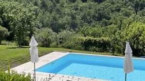 Ein rechteckiger Pool mit zwei weißen Sonnenschirmen, umgeben von einer gefliesten Terrasse und üppiger Bepflanzung.