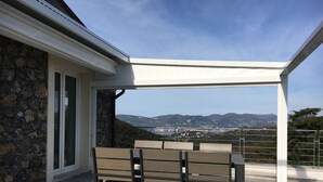 Eine Terrasse mit Steinmauer, einer weißen Markise und Blick auf Stadt und Berge.