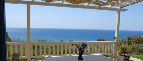 A covered patio with a table and chairs, overlooking the sea.
