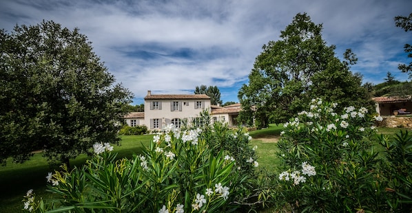 A large, white building with a tiled roof, surrounded by lush greenery and white flowers.