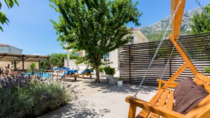 A wooden swing chair with a brown cushion, a pool, and lounge chairs with blue cushions. - Luxury Villa With Pool, Gym, Bicycles And Beautiful Sea View (Kaštel Sucurac)