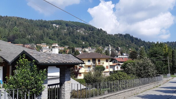 A residential street with houses, a stone wall, and a mountain in the background. - Bianchina💕 (premeno)