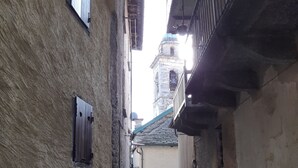 A narrow alleyway with stone walls, a small window, and a bell tower in the distance. - Bianchina💕 (premeno)