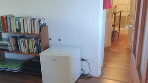 A room with a wooden floor, a white refrigerator, a bookshelf with various books, and a door leading to another room. - Bianchina💕 (premeno)