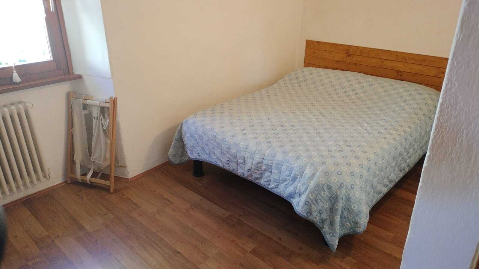 A small, single-bed room with a wooden headboard, a radiator, and a drying rack.