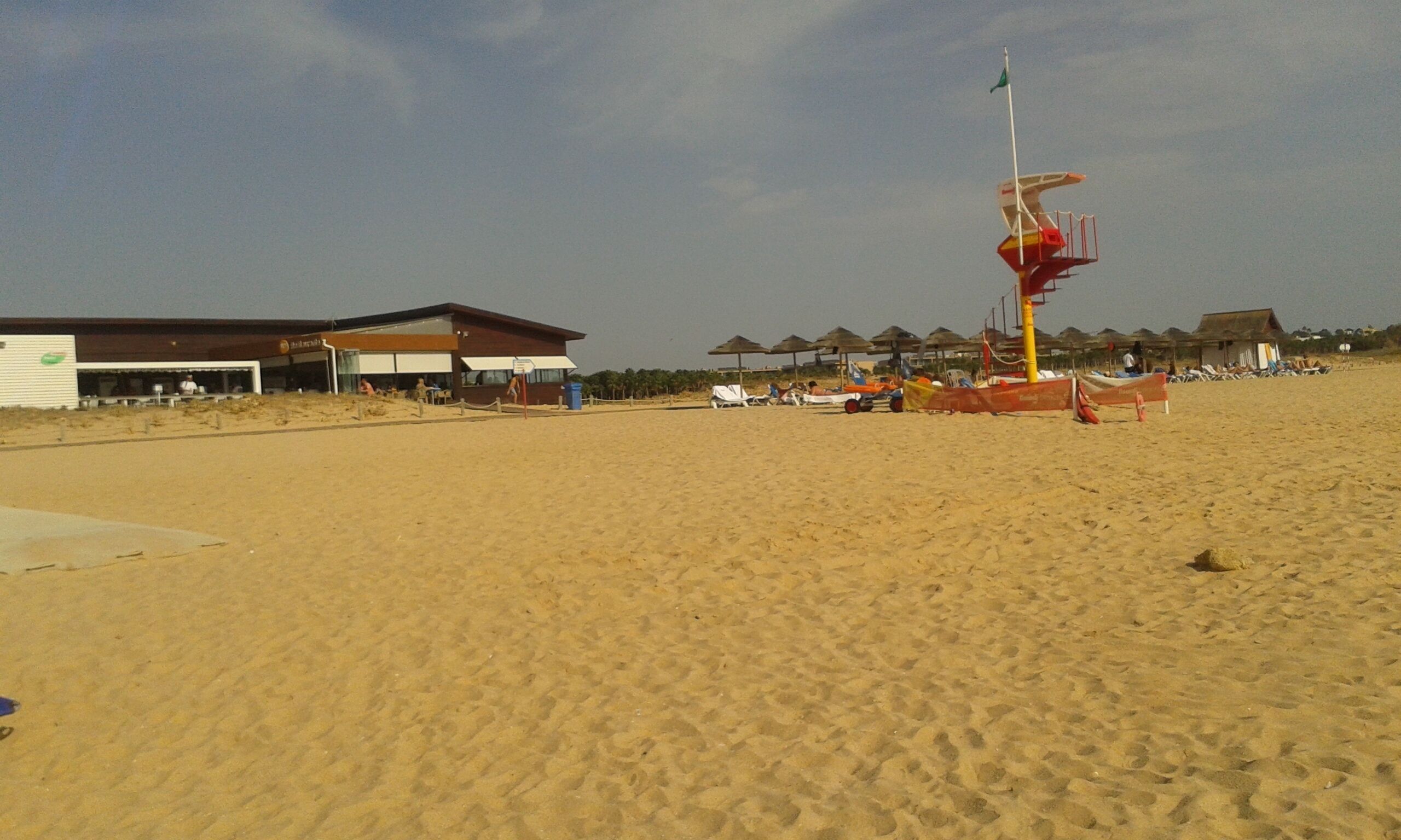 A beach with a lifeguard tower, umbrellas, and beach chairs. There are buildings in the background.