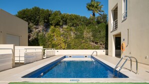 Ein rechteckiger Pool mit blauen Fliesen im Inneren, umgeben von einer beigen Poolterrasse.