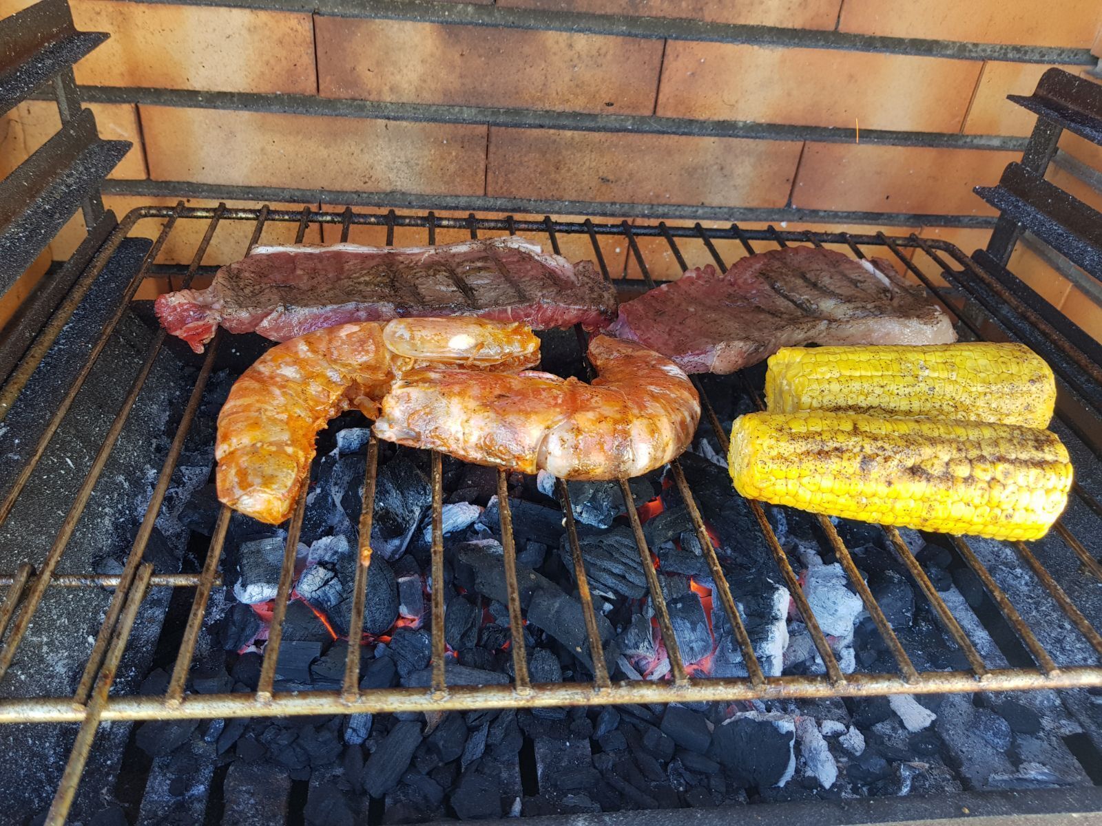 Una griglia con diversi tipi di carne e pannocchie.