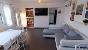 Een ruime woonkamer met een eethoek, een zithoek, een televisie en een boekenkast.