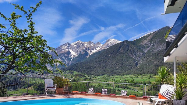 Piscina com vista para as montanhas, área de estar externa e guarda-corpo.
