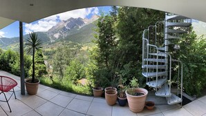 Uma vista panorâmica de uma varanda com escada espiral de metal, plantas em vasos e mobiliário de exterior.