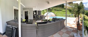 Un área de estar al aire libre cubierta, con vista a la piscina, una mesa de comedor y un sofá.