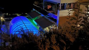 Estrutura ao ar livre em vários níveis, com uma cúpula azul e assentos em terraços, iluminada por luzes de cordão e iluminação ambiente.