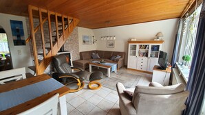 Un salon chaleureux avec un escalier en bois, une cheminée, un canapé, une table basse et un téléviseur posé sur un meuble.