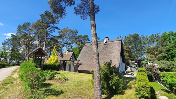 Une maison de campagne avec un toit de chaume, entourée d’arbres et d’un jardin bien entretenu.