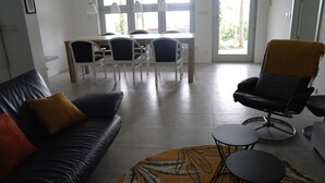 A modern living room with a black leather sofa, a yellow patterned rug, a black armchair, and a dining area with white chairs and a wooden table. - Modern 3 bedroom garden apartment with maximum privacy (Castino bei Alba)