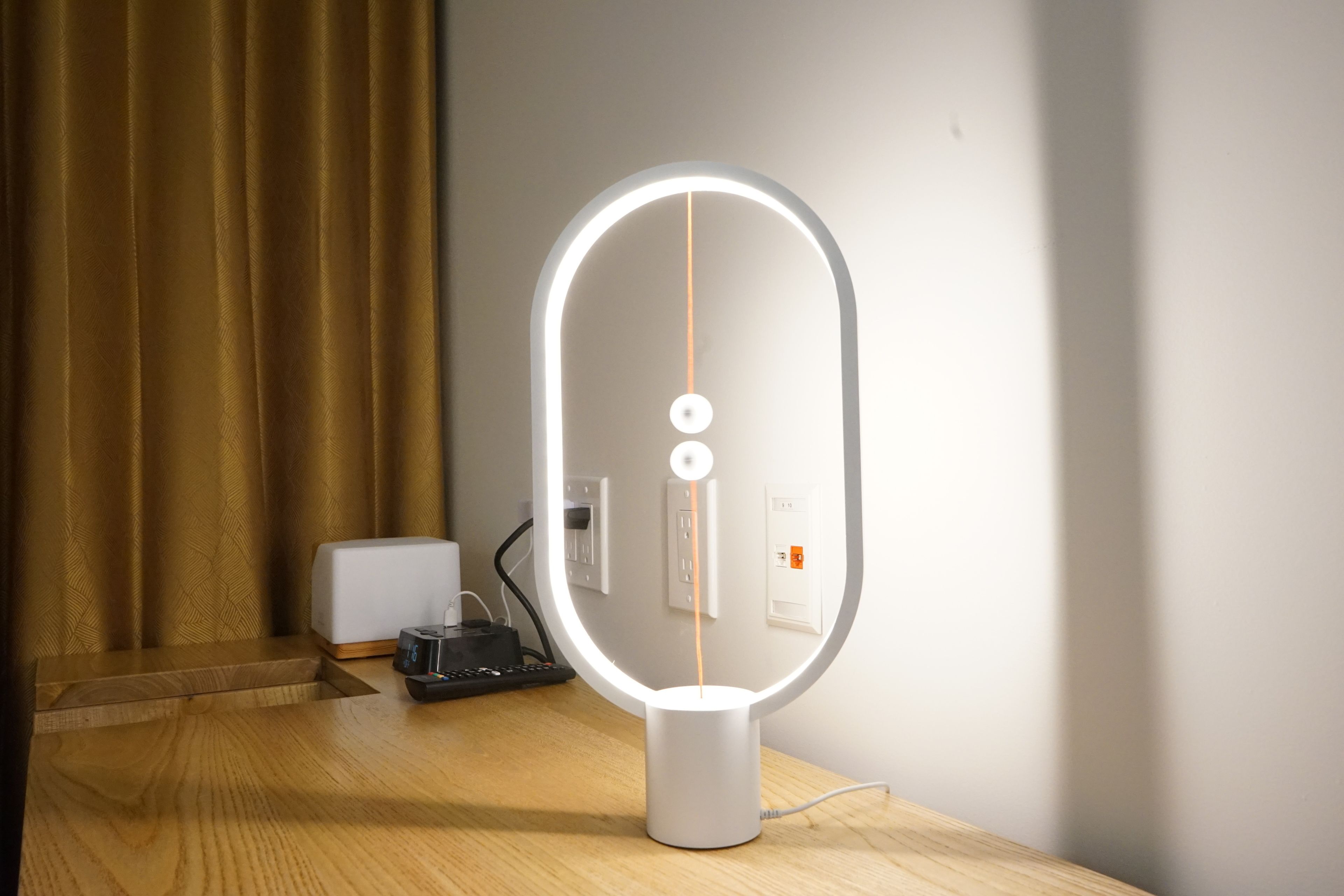 Un miroir de coiffeuse moderne et éclairé, posé sur une surface en bois, avec une prise de courant et une télécommande à proximité.
