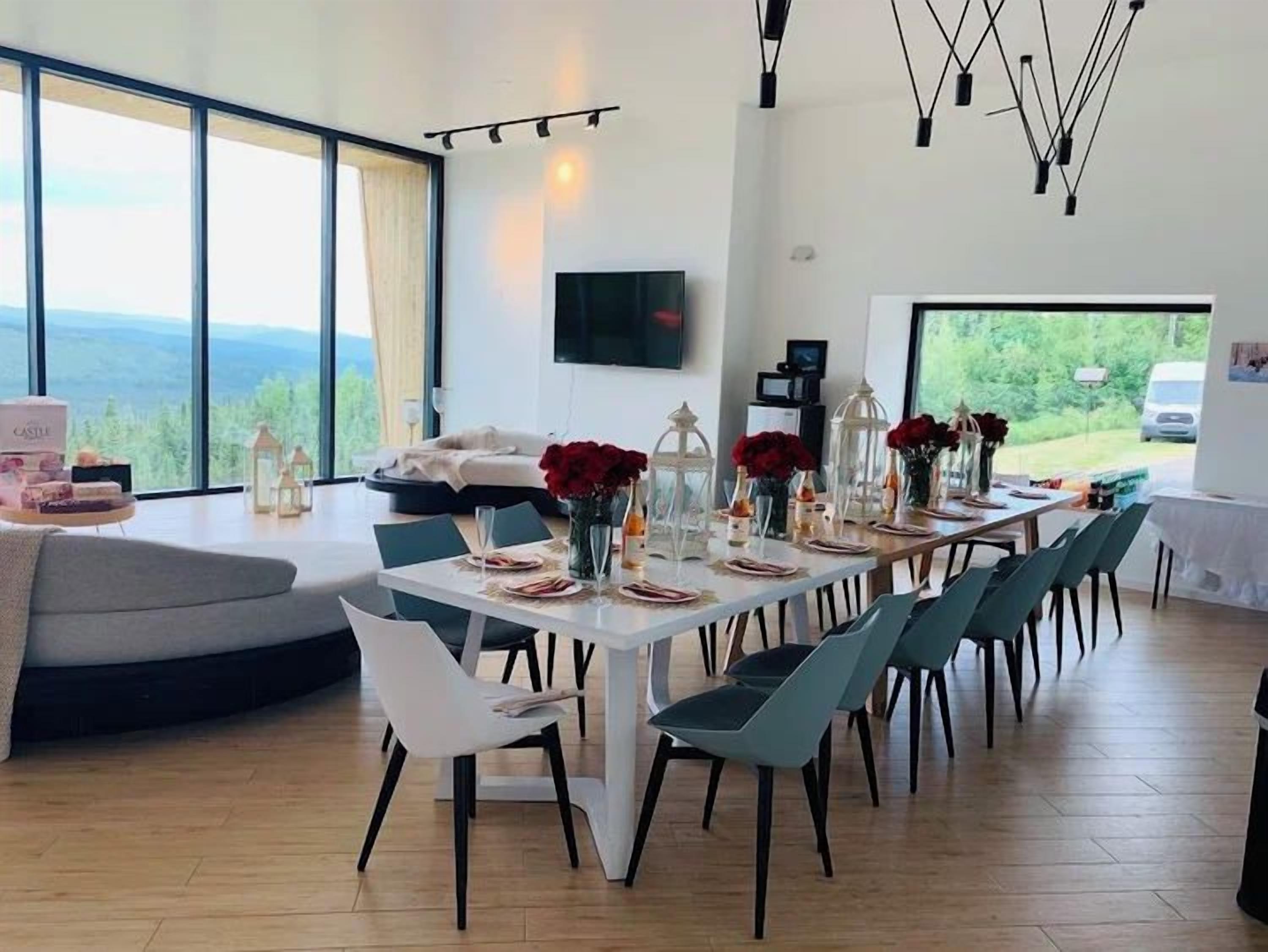 A modern dining area with a long table, chairs, and a view of the outdoors.