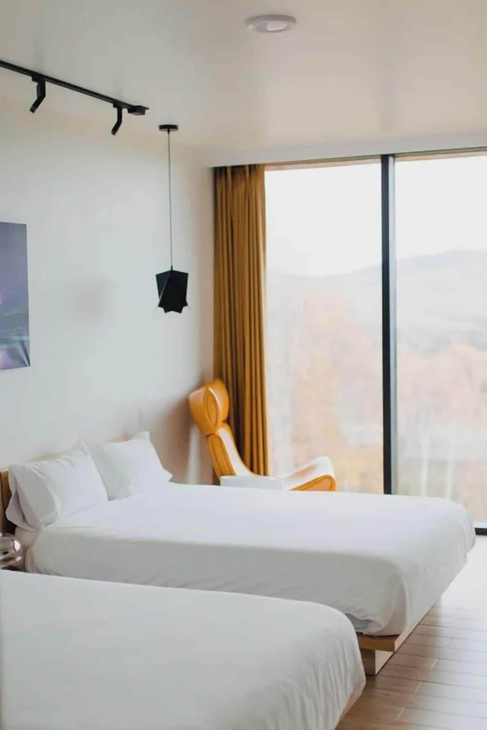 Ein Hotelzimmer mit zwei Betten, einem großen Fenster mit Blick, einer Pendelleuchte und einem Sessel.