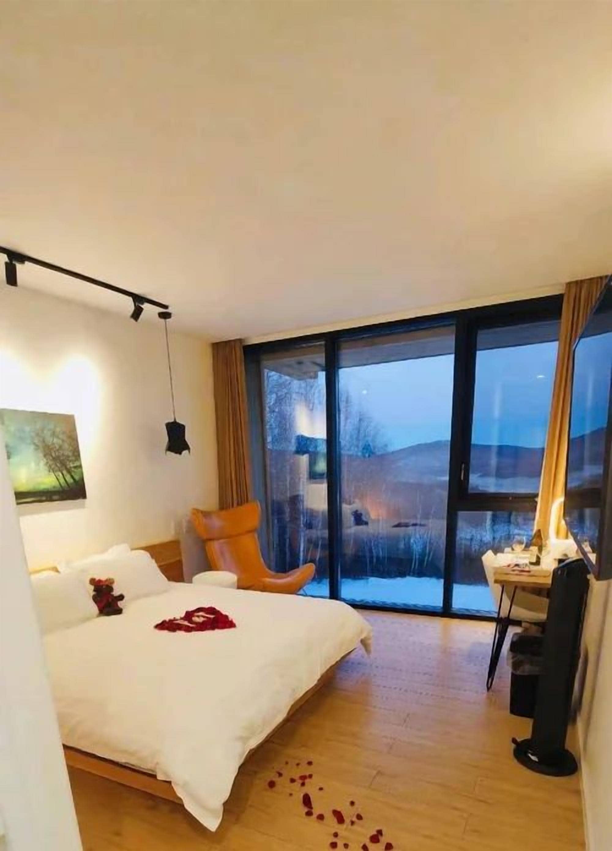 A modern hotel room with a large bed, a desk, and a view of the outdoors through a sliding door.