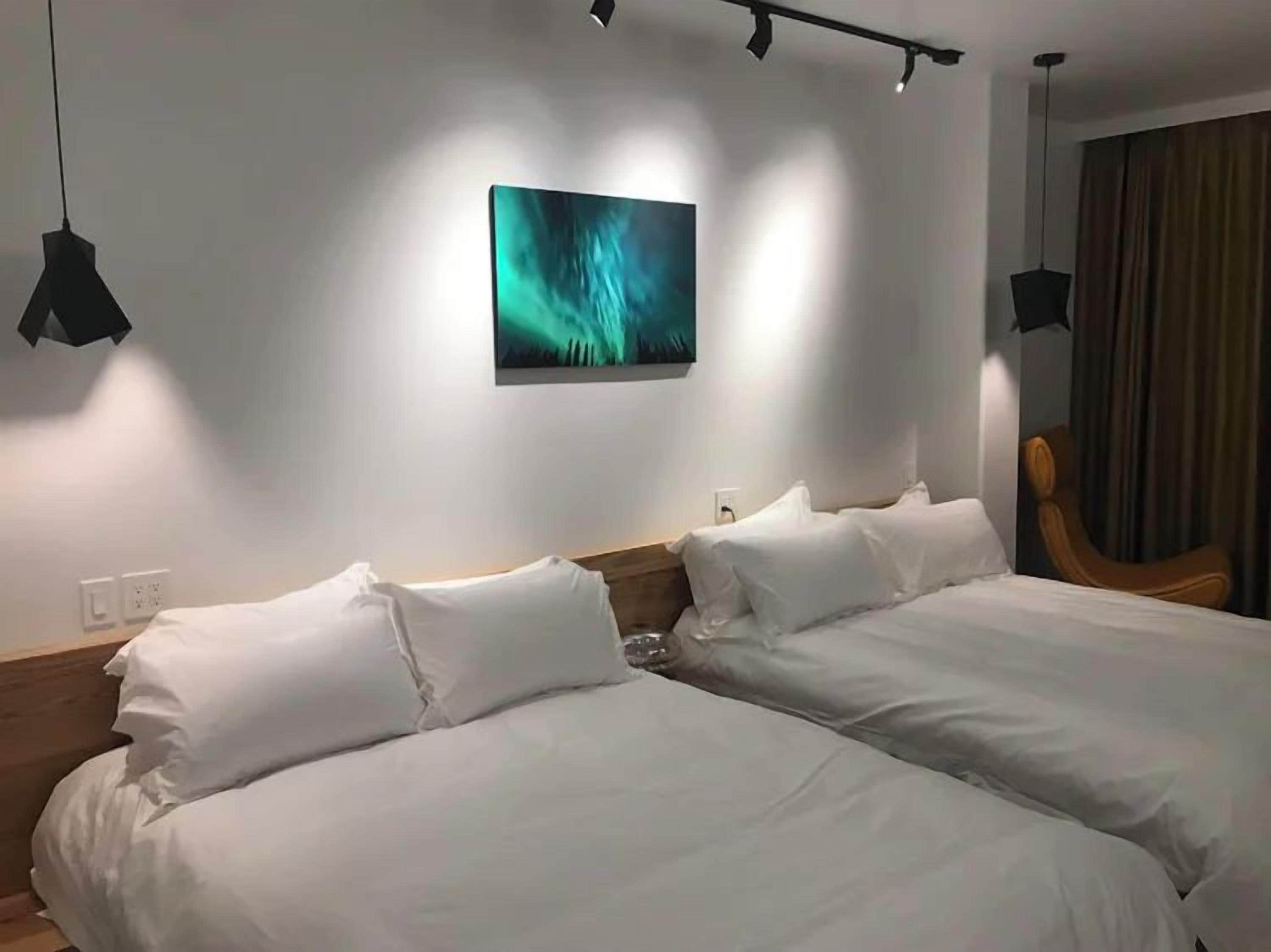 A hotel room with two beds, a painting on the wall, and a chair.