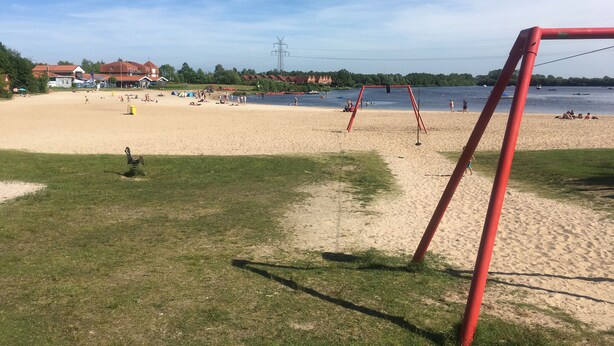 En strand med en röd gunga, en sandstrand och ett lugnt vattenområde i bakgrunden.