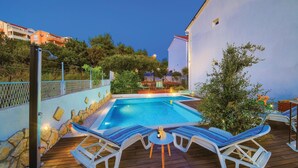 A swimming pool with lounge chairs and a small table, surrounded by a wooden deck and a stone wall. - Gorgeous apartment in Okrug Gornji (Okrug Gornji)