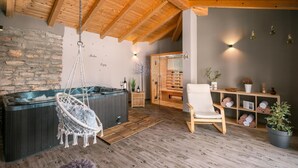 Une salle de spa avec un plafond en bois, un mur en pierre, un jacuzzi, un fauteuil de massage et une étagère avec des serviettes et des plantes.