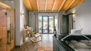 Un intérieur moderne avec un plafond en bois, un sauna, un fauteuil suspendu et une vue sur un espace extérieur aménagé avec des chaises longues.
