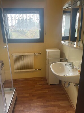 A bathroom with a white sink, a mirror, a radiator, and a window with curtains. - Very nice apartment with a large sun terrace (Stadtkyll)