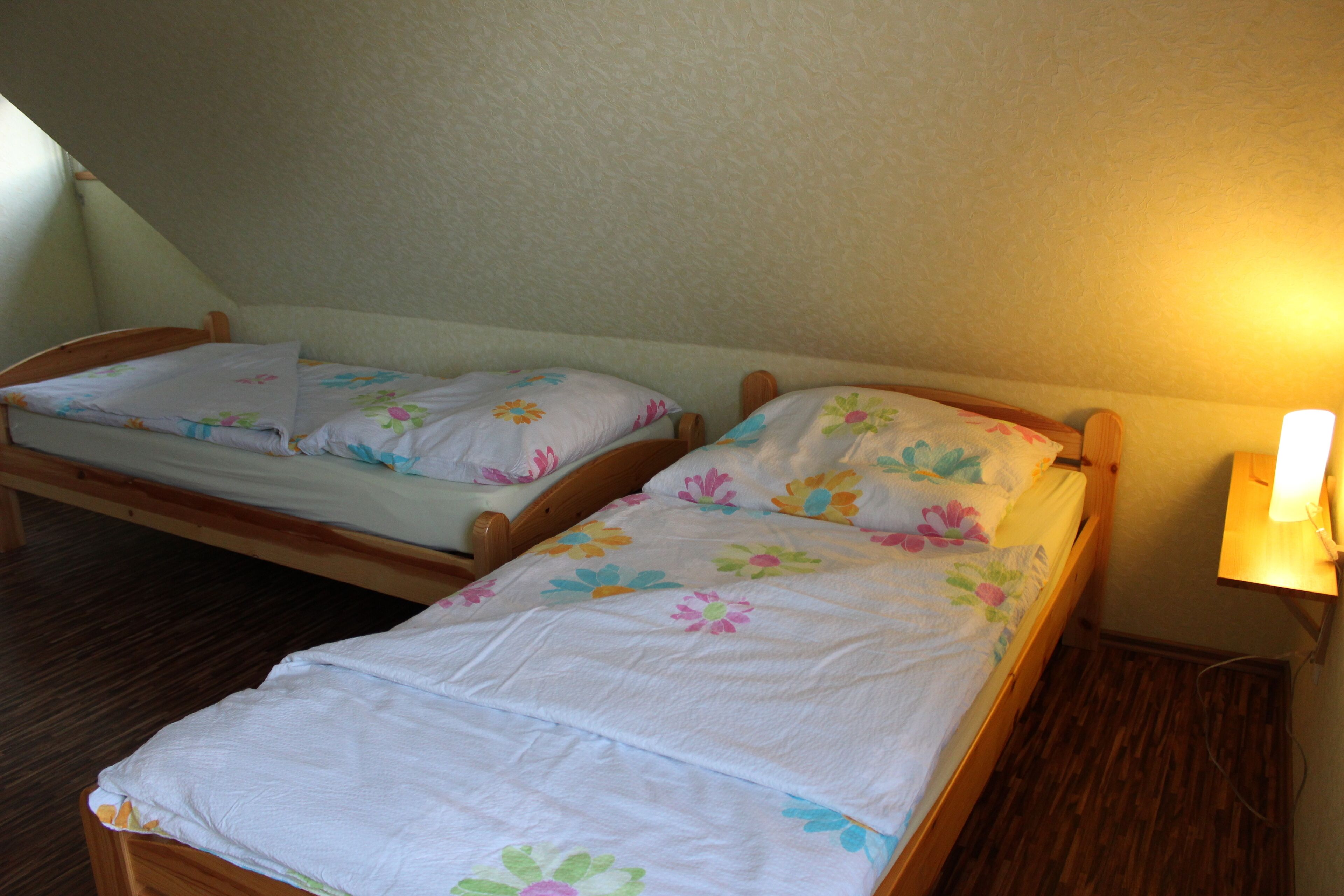 Twee enkele bedden met bloemenbedrukking in een kamer met houten vloer en een schuine plafond.