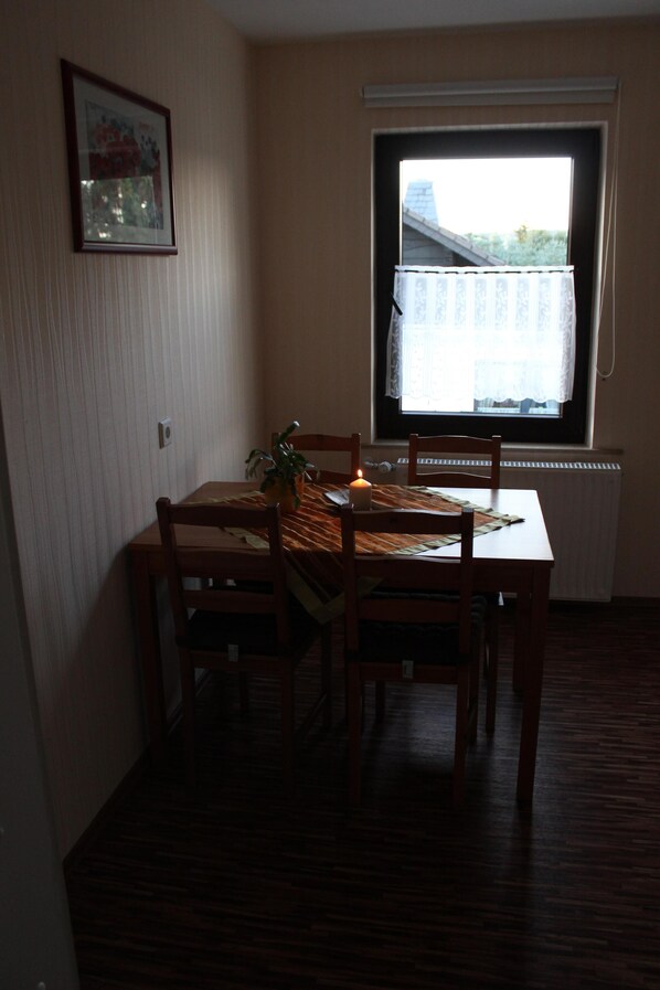 A dining area with a table, chairs, a candle, and a window with a view of a building and trees. - Very nice apartment with a large sun terrace (Stadtkyll)