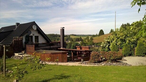 A house with a wooden deck, a chimney, and a view of a green landscape. - Very nice apartment with a large sun terrace (Stadtkyll)