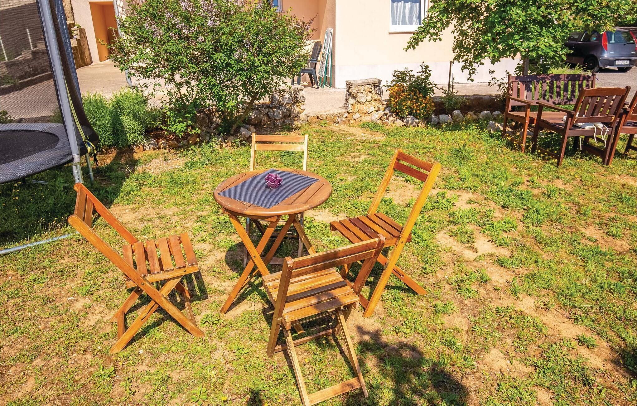 An outdoor seating area with a round table and four wooden chairs, surrounded by a grassy lawn and a stone wall.
