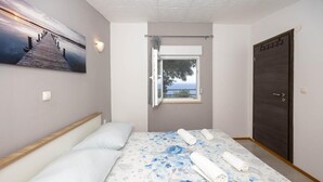 A bedroom with a bed, a window with a view, a door, and a wall-mounted light fixture.