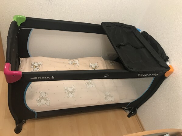Una cuna de viaje convertible con estructura negra y un cojín color beige con diseños de ositos de peluche.