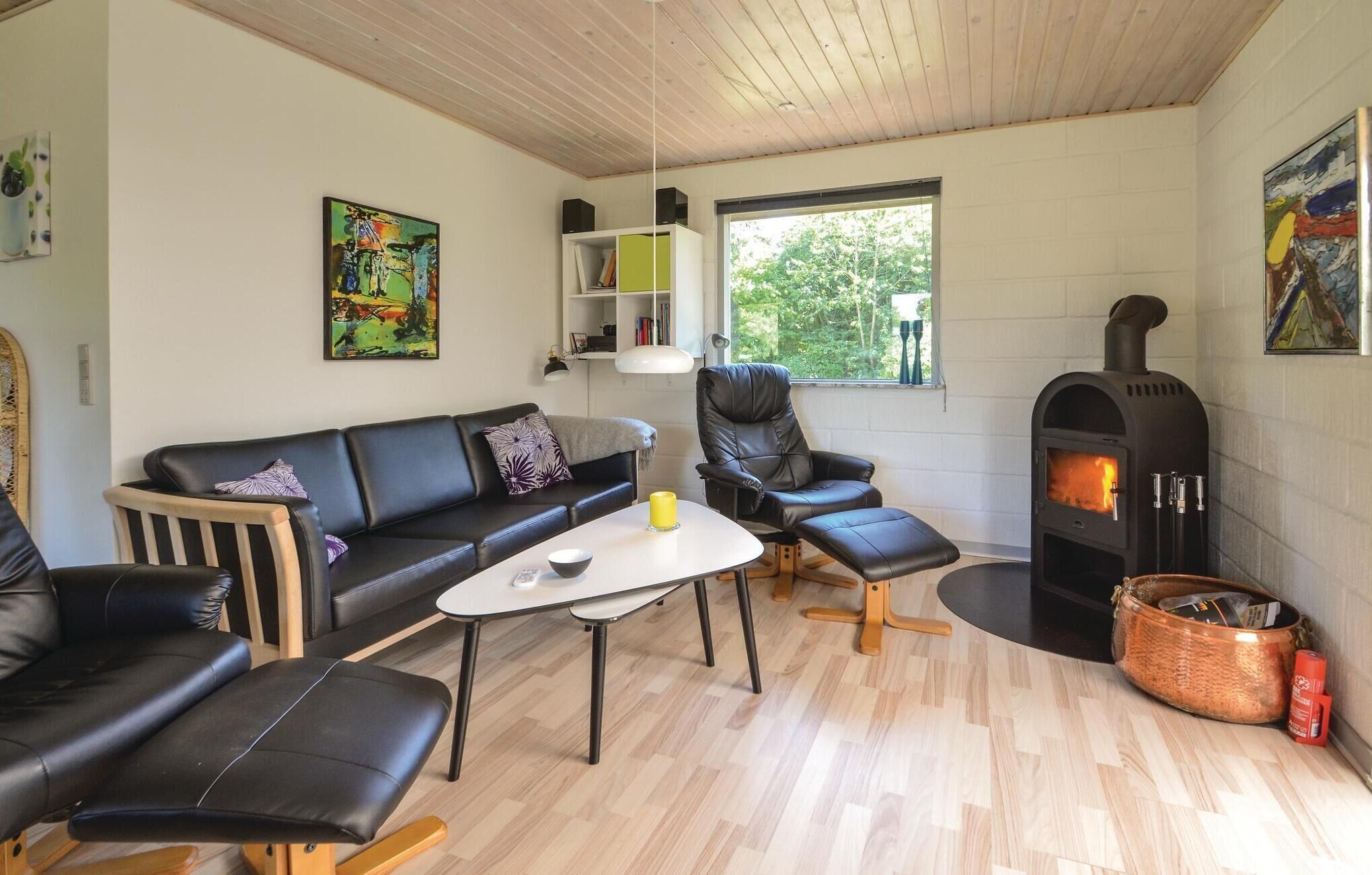 A cozy living room with a black leather sofa, a black leather chair, a small white table, and a wood-burning stove.