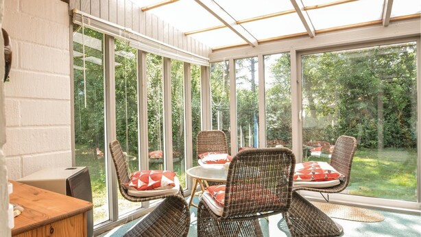 A sunroom with large windows, wicker furniture, and a view of a garden. - 3 bedroom stunning home in Hjerm (Hjerm)