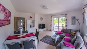 A living room with a dining area, a television, and a large window with curtains. - Barrier-free relaxation in a quiet location near the Elbe, the Altmarkt (Sandau/Elbe)