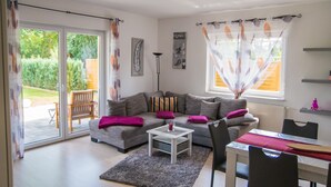 A modern living room with a grey sofa, a coffee table, and a dining area with a table and chairs. - Barrier-free relaxation in a quiet location near the Elbe, the Altmarkt (Sandau/Elbe)