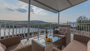 Ein überdachter Außenbereich mit Korbmöbeln, einem Glastisch mit Früchten und Weingläsern und Blick auf die Landschaft.